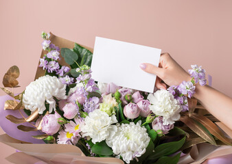 Womens hand holding blank paper card and beautiful bouquet of mixed flowers. Love, Birthday, Valentines day concept. closeup