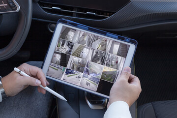 Man holding digital tablet with multiple camera views of office locations while sitting in car....