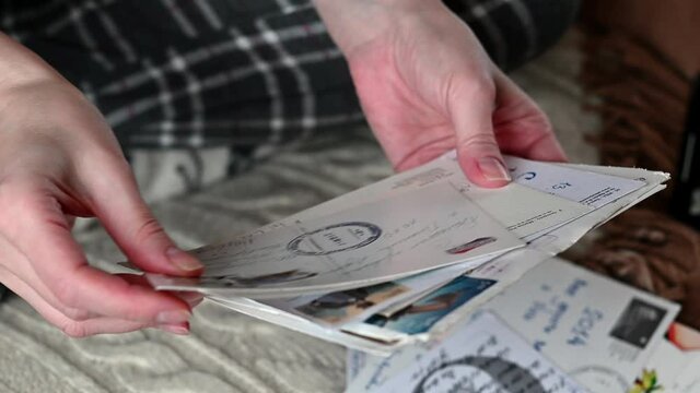 Woman selects old paper post cards sitting on sofa, hands close up.