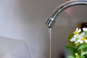 In selective focus water running from a metal faucet in kitchen area with wall background 