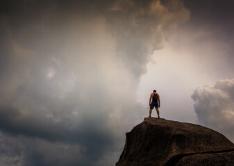 Young man standing on big stone overlooking a dramatic cloudy sky. Travel and adventure concept
