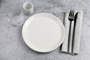 Minimalistic table setting with empty plate, glass, fork and knife on gray background. Top view.