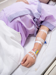 saline solution on hand of women patient in pink clothes lying on the hospital bed