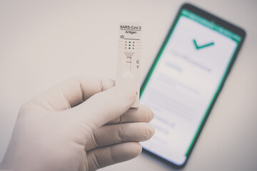 Closeup view of gloved hand with SARS-CoV-2 rapid antigen test nasal and phone with green digital certificate on display. Health, healthcare, corona virus, pandemic, illness, disease, travel concept