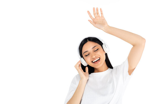 Joyful Asian Woman In Headphones Dancing With Closed Eyes Isolated On White.