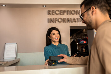Guest pays for the stay at the hotel to female receptionist with a smart phone at the reception.