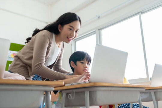 Asian woman teacher is teaching little boy learning on laptop
