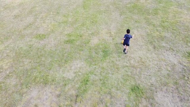 Boy playing soccer. Boy running after a ball on soccer field. Concept of constancy, freedom, play, determination. Sport. Child playing alone. Running boy. Drone image. Filming from the air.