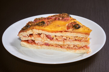 A piece of the three-layer homemade pizza with cheese, sausages, ham and olives. Close-up, selective focus.