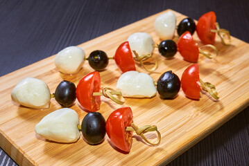 Canapes on bamboo skewers made of mozzarella balls, olives, cherry tomatoes on a wooden board.