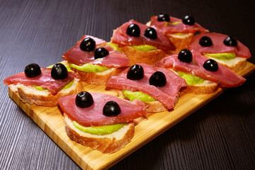 Homemade bread sandwiches with salmon fillet, avocado sauce and olives. A funny snack.