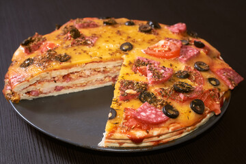 Three-layer cut-out homemade pizza with cheese, sausages, ham and olives. Close-up, selective focus.