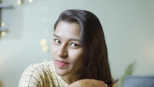 Close up shot of happy Young woman combing her hair by looking camera at home - concept of haircare, welness and leisure activity.