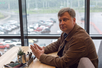 Portrait of an adult man in a corduroy jacket waiting order at a table in a cafe.