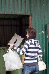 A woman striped sweatshirt and jeans throws out a package of household garbage.