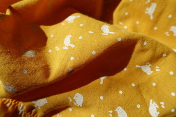 Soft folds on amber yellow cotton fabric with birds print