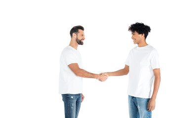happy interracial men in t-shirts and jeans looking at each other and shaking hands isolated on white.