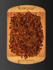 Raisins on a wooden board for the background. Isolated over black background