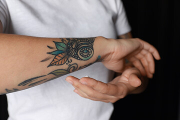 Woman applying cream on her arm with tattoos against black background, closeup