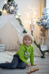 Cute toddler blond child in front of a teepee, playing with wooden train, lying on the floor