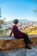 Fototapeta na wymiar A young tourist sitting in spring looking at the views of the city and the Cathedral of the Incarnation of Malaga from the Castillo de Gibralfaro in the city of Malaga, Andalusia. Spain
