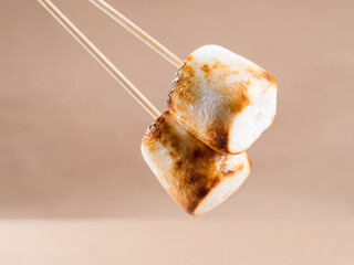 Two sweet marshmallows with baked crust on a brown background.