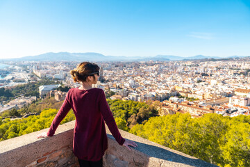 Naklejka premium A young woman admiring the beautiful city from the wall of the Gibralfaro Castle in the city of Malaga, Andalusia. Spain