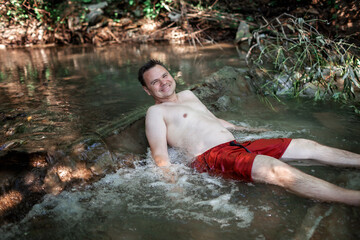 Happy middle aged man resting in stream canyon river in the mountains, nature pool. Cold water, hardening and natural spa procedure, wildlife and green tourism, active healthy lifestyle, summertime