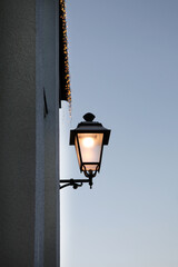 a nostalgic lamp on the wall, an old street lamp made of metal and with beautiful curved elements. It has a black color and is attached to a yellow wall.