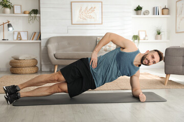 Handsome man doing side plank exercise on yoga mat at home