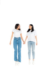 full length view of astonished interracial women holding hands and looking at each other while levitating isolated on white.
