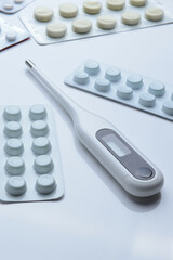 tablets in a package and a white electronic thermometer on a white surface close-up.