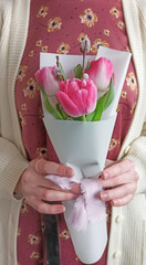 Spring bouquet of three pink tulips with twigs, wrapped in white paper. Holding in woman hands. Florist lifestyle.