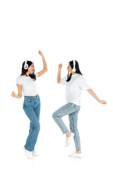 full length view of excited multiethnic women in headphones dancing on white.