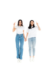 Obraz premium full length view of cheerful multiethnic women pointing with fingers while levitating isolated on white.