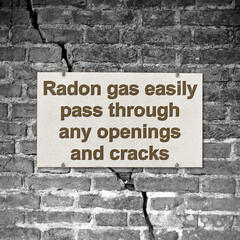 A cracked brick wall with warning message abaut radon gas escaping through cracks and openings - concept image