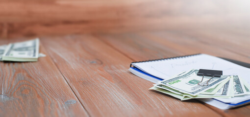 dollars lie on top of a notebook on a wooden table