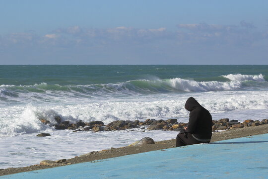 A Lonely Silhouette Of A Man In Black Against The Background Of A Swaying Sea