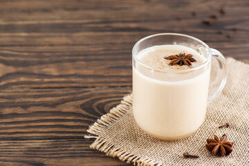 Masala tea with milk, cloves and anise in a glass mug on a wooden table. Horizontal orientation, copy space.