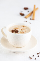 Masala tea with milk, ginger root and spices in a mug on a table.