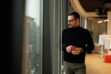 Serious adult manager, gazing through the window, while having a cup of coffee.