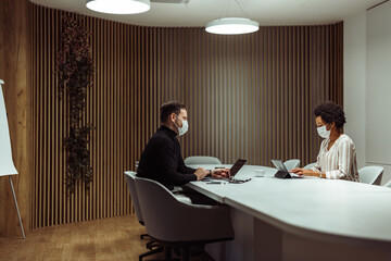 Busy caucasian man with a mask, checking the company budget with his assistant.