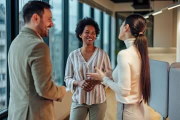 Smiling group of coworkers, talking about their weekends before starting work.