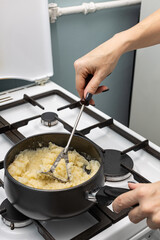 a woman's hand crumples boiled potatoes with a kitchen appliance