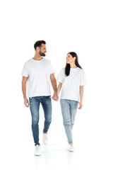 Obraz premium full length view of happy interracial couple looking at each other and holding hands while walking on white.
