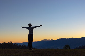 Silhouette of young girl doing yoga in the mountains at sunset sky background
