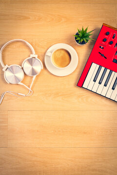 top view of red synthesizer keyboard, cup of coffee, potted plant and white headphone on wooden desk. music background concept
