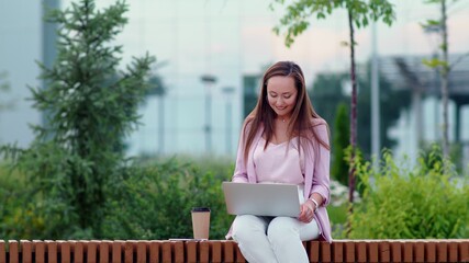 A young woman is sitting at a computer on the street and drinking coffee. Business woman