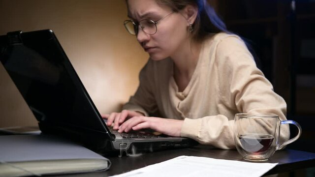 A young woman's old laptop starts to smoke while she is working. She panics and starts fanning the smoke