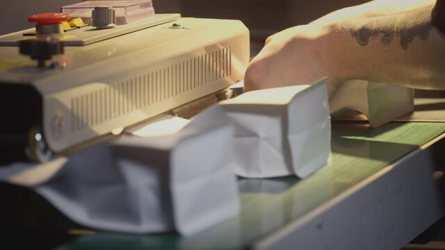 Packaging of roasted brown coffee in a zip pack. Conveyor belt for industrial coffee production. Filling machine. A man packs coffee in a bag